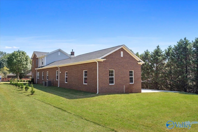 view of side of home with cooling unit, brick siding, a lawn, and a chimney