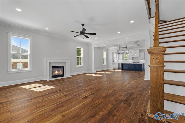 unfurnished living room featuring crown molding, dark wood finished floors, a wealth of natural light, a premium fireplace, and stairs