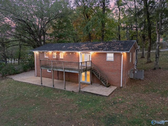 back house at dusk with a yard, a wooden deck, a patio area, and central air condition unit