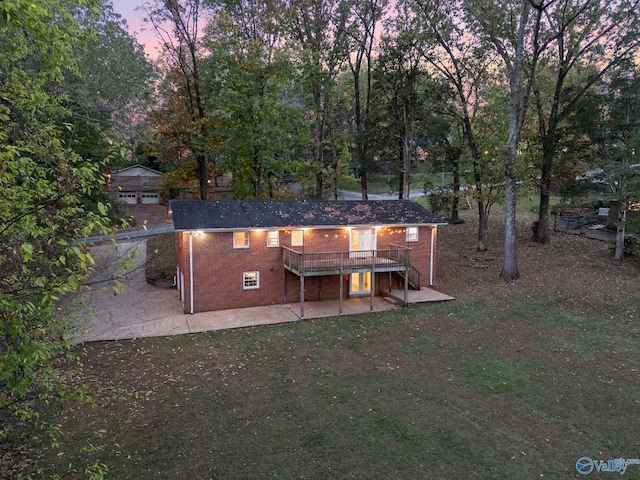 back house at dusk featuring a lawn, a wooden deck, and a patio