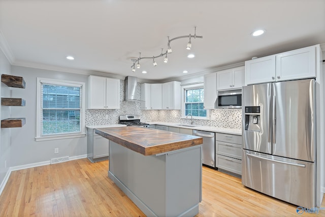 kitchen featuring wall chimney exhaust hood, wood counters, crown molding, a kitchen island, and appliances with stainless steel finishes