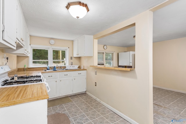 kitchen with range, plenty of natural light, white refrigerator, and white cabinets