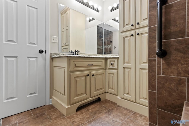 full bath featuring a tile shower, stone finish flooring, and vanity