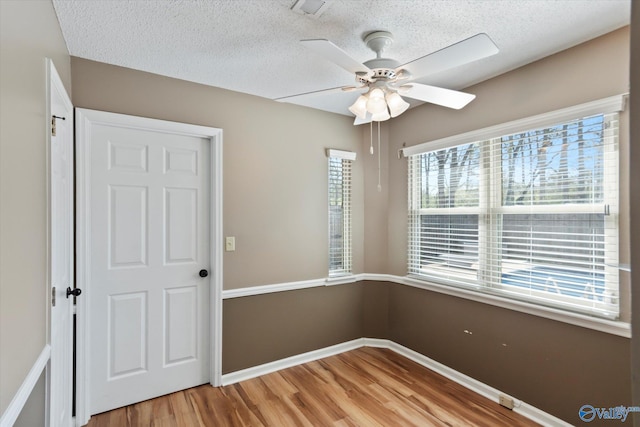 empty room with a ceiling fan, a textured ceiling, light wood-type flooring, baseboards, and visible vents