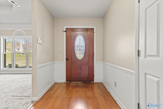 carpeted foyer with baseboards, visible vents, wood finished floors, and a textured ceiling