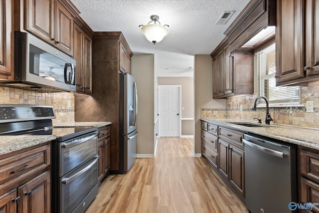 kitchen featuring visible vents, light wood finished floors, stainless steel appliances, a sink, and light stone counters