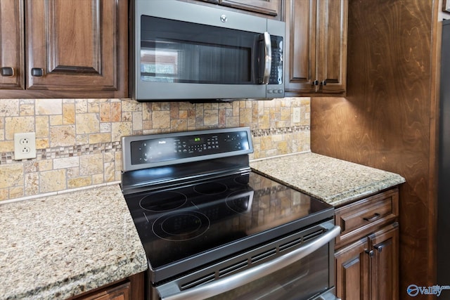 kitchen featuring dark brown cabinetry, light stone countertops, tasteful backsplash, and appliances with stainless steel finishes