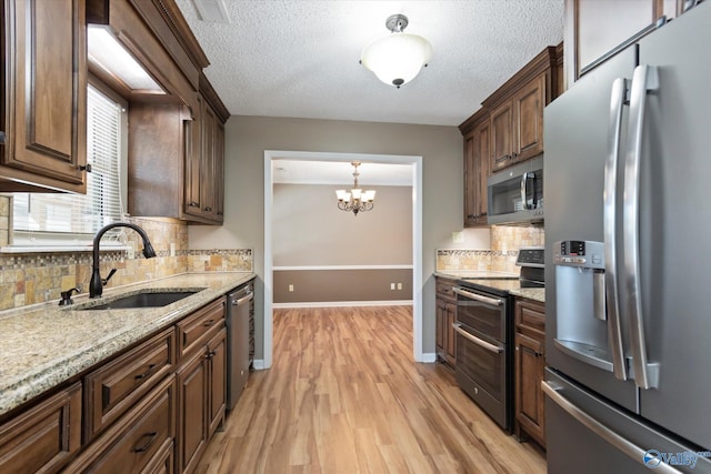 kitchen with light wood-type flooring, an inviting chandelier, a sink, light stone countertops, and appliances with stainless steel finishes
