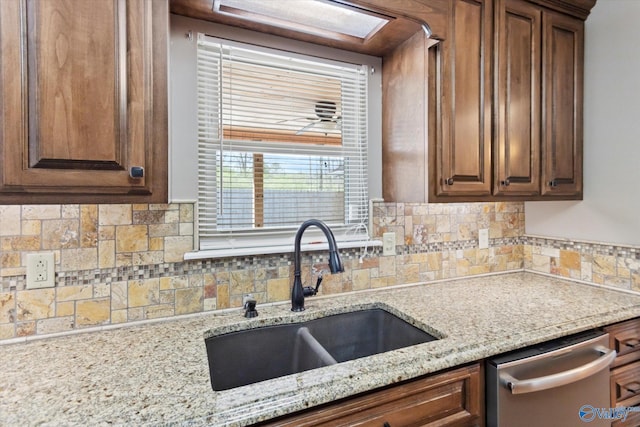 kitchen with backsplash, a sink, stainless steel dishwasher, and light stone countertops