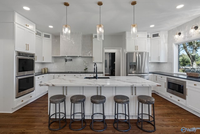 kitchen with white cabinets, a kitchen island with sink, appliances with stainless steel finishes, and dark hardwood / wood-style floors