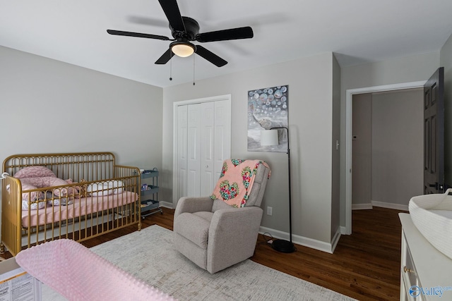 bedroom with a closet, a crib, dark hardwood / wood-style flooring, and ceiling fan