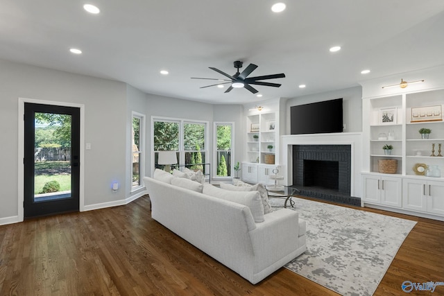 living room with ceiling fan, a fireplace, a wealth of natural light, and dark wood-type flooring