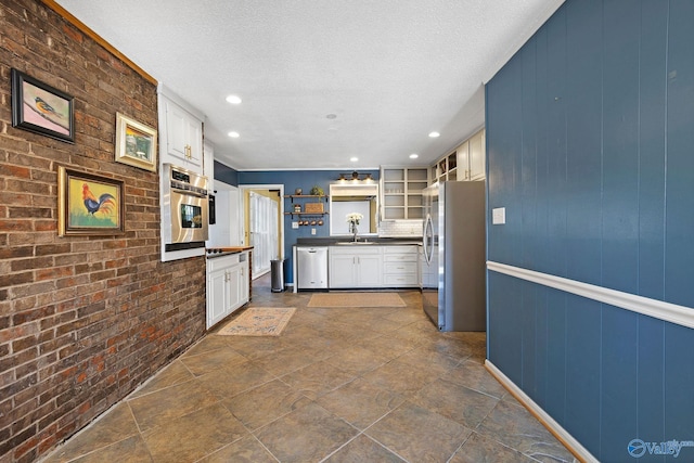 kitchen featuring open shelves, stainless steel appliances, dark countertops, a sink, and brick wall