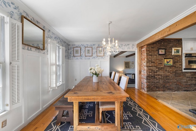 dining area with wallpapered walls, hardwood / wood-style flooring, a wainscoted wall, crown molding, and a fireplace