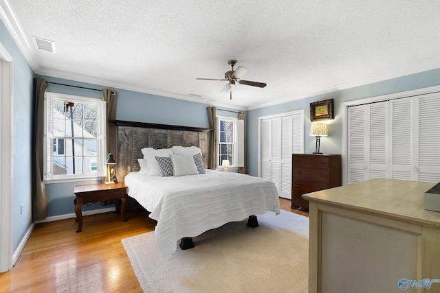 bedroom featuring light wood finished floors, two closets, visible vents, and crown molding