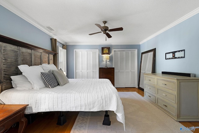 bedroom with visible vents, a ceiling fan, crown molding, light wood-style floors, and multiple closets