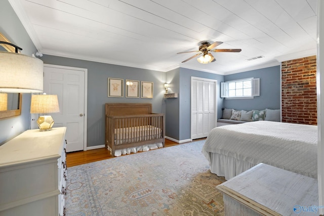 bedroom with wood finished floors, visible vents, baseboards, a closet, and crown molding