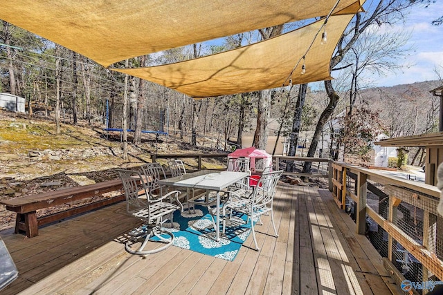 wooden terrace with outdoor dining area, a trampoline, and a mountain view