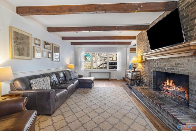 living room featuring a brick fireplace, beamed ceiling, and wood finished floors