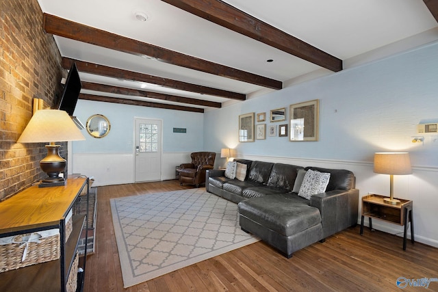 living room with wainscoting, wood-type flooring, brick wall, and beam ceiling