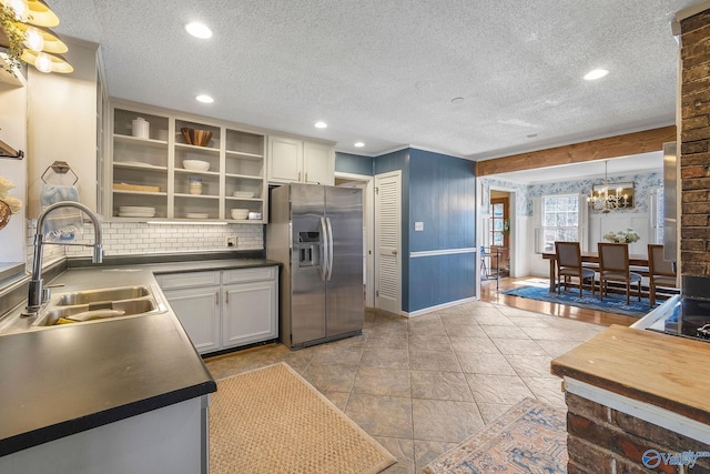 kitchen featuring a sink, stainless steel refrigerator with ice dispenser, backsplash, open shelves, and dark countertops