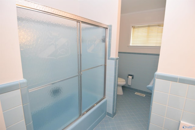 bathroom featuring combined bath / shower with glass door, tile walls, tile patterned flooring, toilet, and crown molding