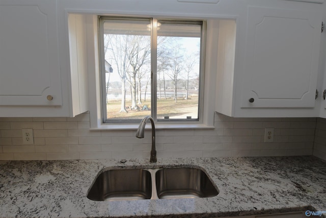 kitchen featuring white cabinetry, light stone countertops, sink, and a wealth of natural light