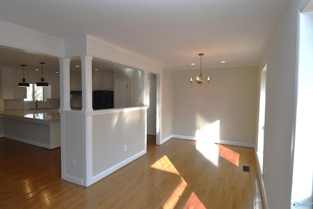 interior space with a notable chandelier, crown molding, wood-type flooring, and kitchen peninsula