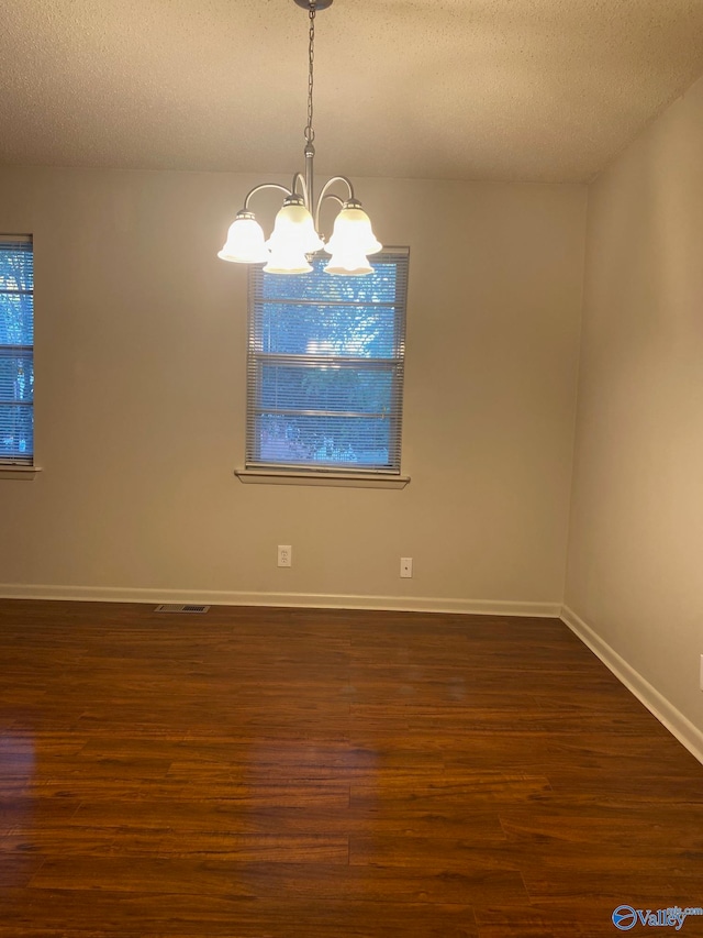 unfurnished room featuring a chandelier, a textured ceiling, and dark hardwood / wood-style floors