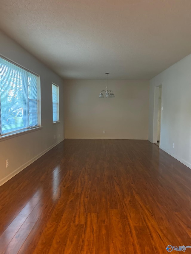 unfurnished room with a textured ceiling, dark hardwood / wood-style flooring, and a notable chandelier