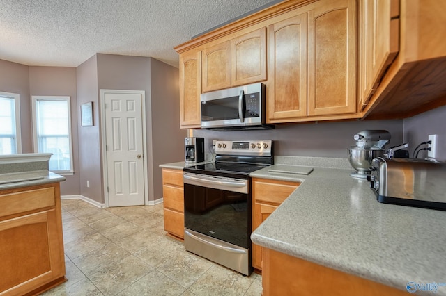 kitchen featuring appliances with stainless steel finishes, a textured ceiling, light countertops, and baseboards