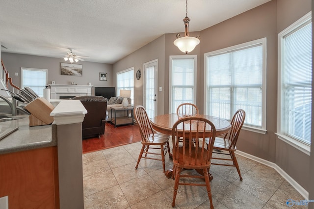 dining room featuring light tile patterned floors, a ceiling fan, baseboards, a fireplace, and a textured ceiling