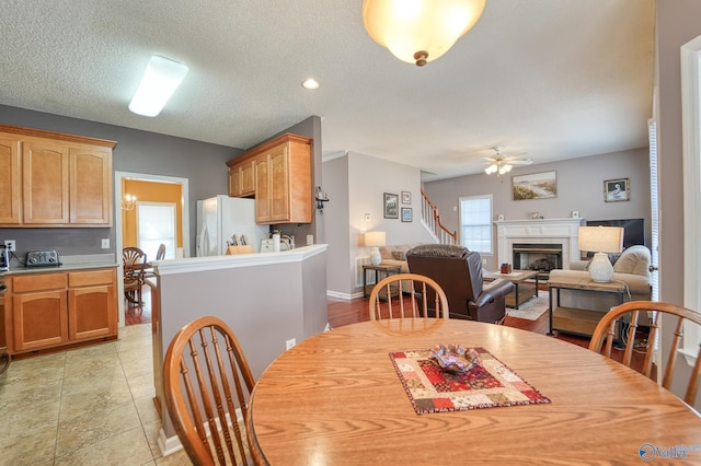 dining area featuring a toaster, light tile patterned flooring, a glass covered fireplace, a textured ceiling, and a ceiling fan