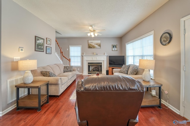 living room with visible vents, ceiling fan, a tiled fireplace, wood finished floors, and a textured ceiling