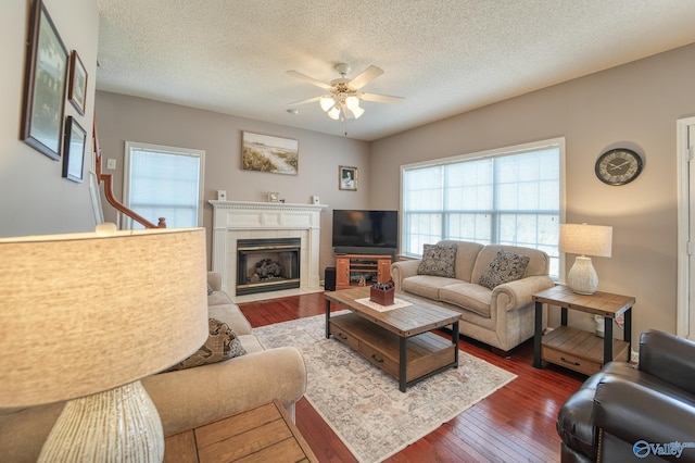 living area featuring dark wood-style floors, a tile fireplace, a textured ceiling, and a ceiling fan