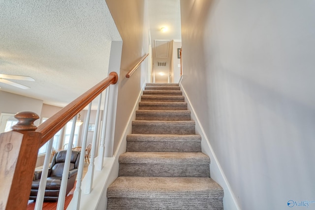 stairs featuring baseboards, a textured ceiling, and a ceiling fan