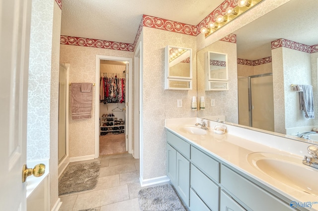 full bath featuring wallpapered walls, a textured ceiling, a stall shower, and a sink