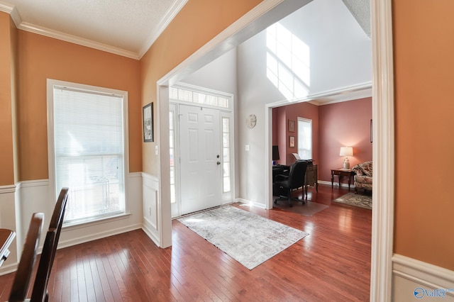 foyer entrance featuring hardwood / wood-style floors, a textured ceiling, a wainscoted wall, and ornamental molding