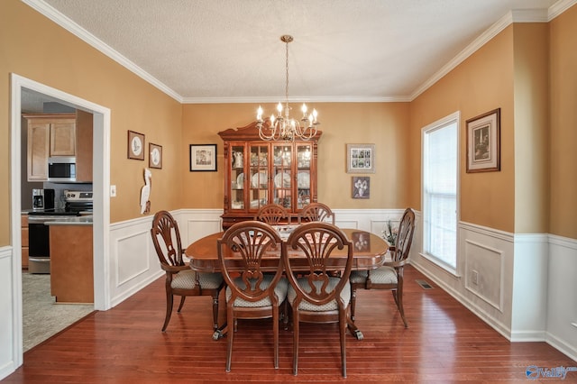 dining room featuring dark wood finished floors, a notable chandelier, wainscoting, and crown molding