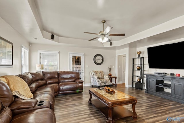 living room with a raised ceiling, ceiling fan, and dark hardwood / wood-style flooring