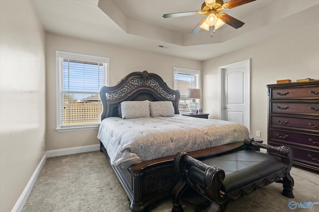 bedroom with light colored carpet, multiple windows, a tray ceiling, and ceiling fan