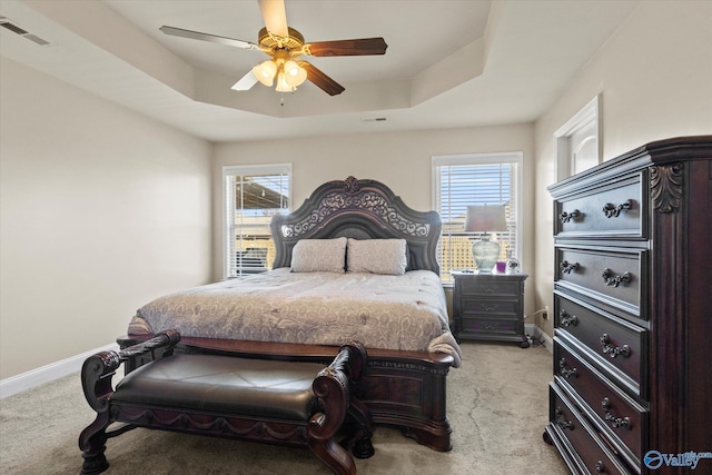 carpeted bedroom featuring ceiling fan, a tray ceiling, and multiple windows