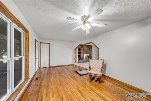 sitting room featuring ceiling fan, wood-type flooring, a textured ceiling, and a fireplace