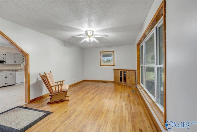 unfurnished room with a textured ceiling, light wood-type flooring, and ceiling fan