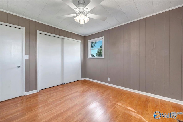 unfurnished bedroom with crown molding, wooden walls, light wood-type flooring, and ceiling fan