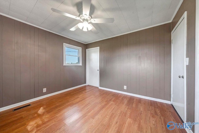 unfurnished bedroom featuring light hardwood / wood-style flooring, wooden walls, and ceiling fan