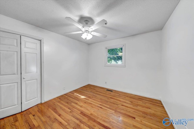 unfurnished bedroom featuring light hardwood / wood-style flooring, a textured ceiling, a closet, and ceiling fan