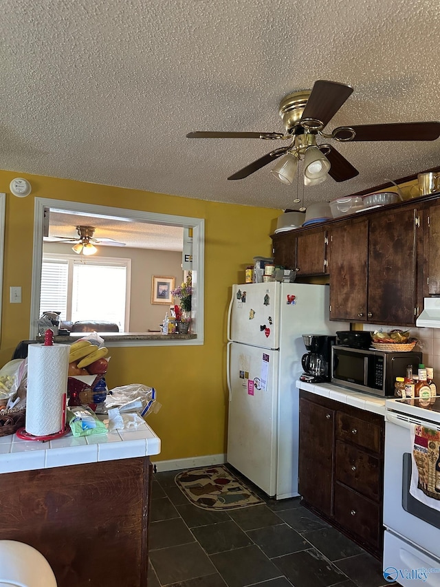 kitchen with a ceiling fan, exhaust hood, tile countertops, white appliances, and dark brown cabinets