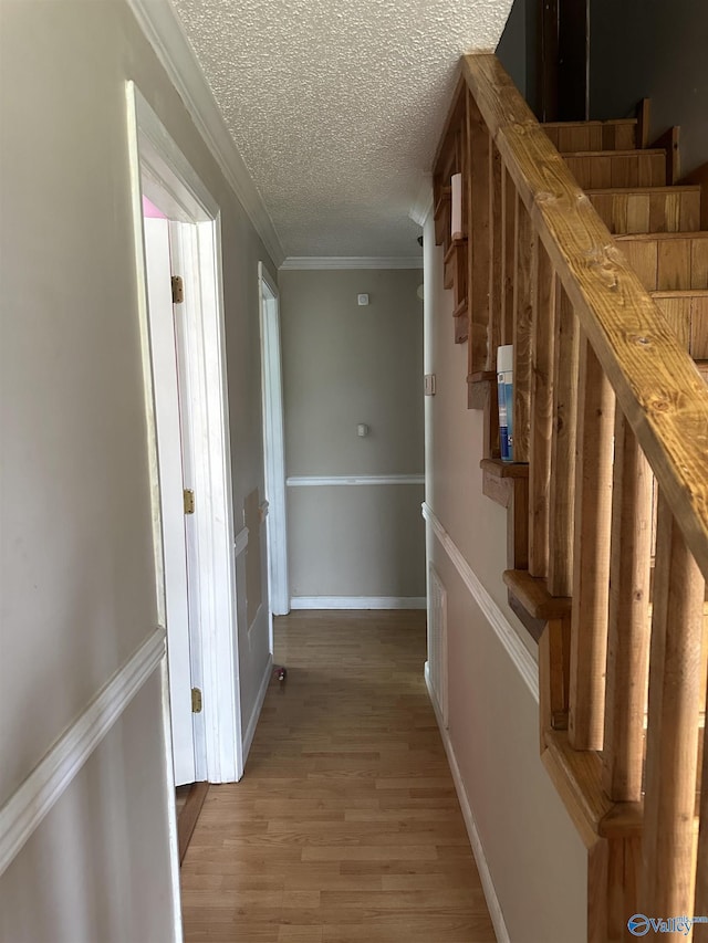 hallway featuring crown molding, stairway, a textured ceiling, baseboards, and light wood-style floors