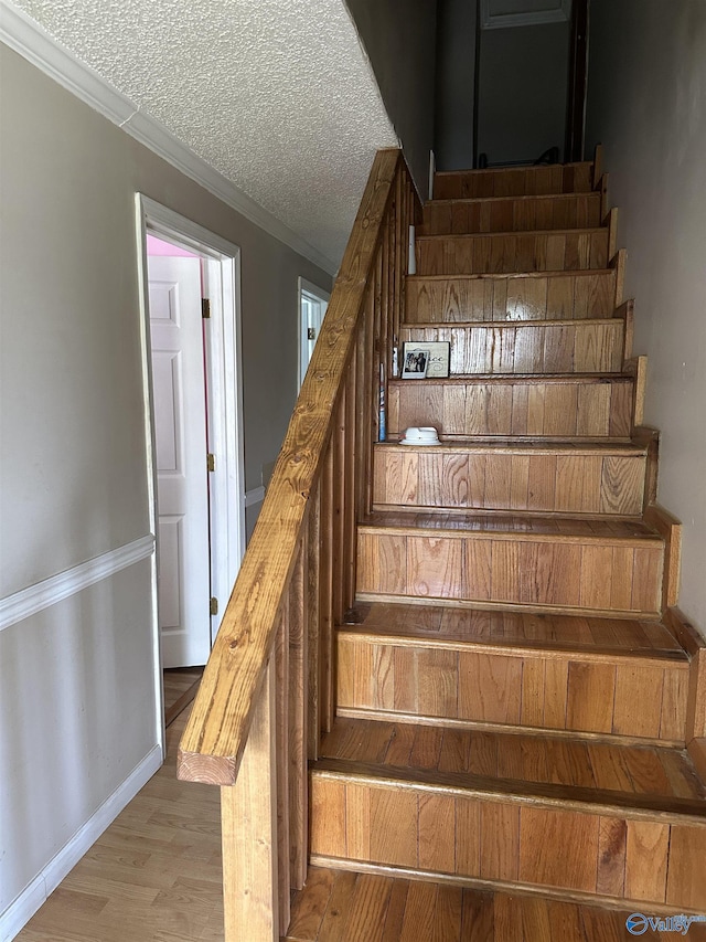 staircase featuring baseboards, crown molding, wood finished floors, and a textured ceiling